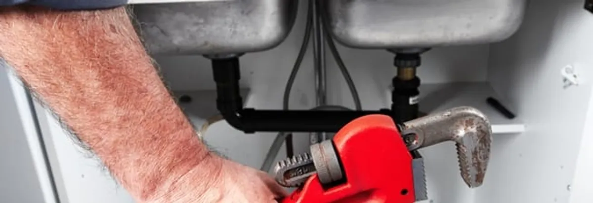 Garbage disposal repair technician tightening drain connections under a kitchen sink in Tucson, AZ