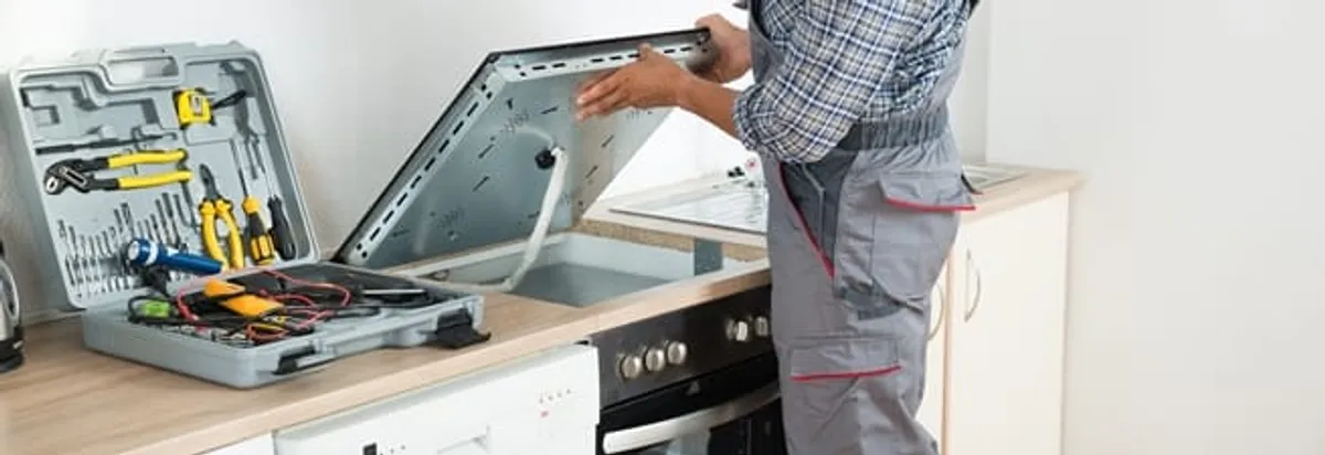 Cooktop repair technician lifting a built-in stovetop for service in Tucson, AZ